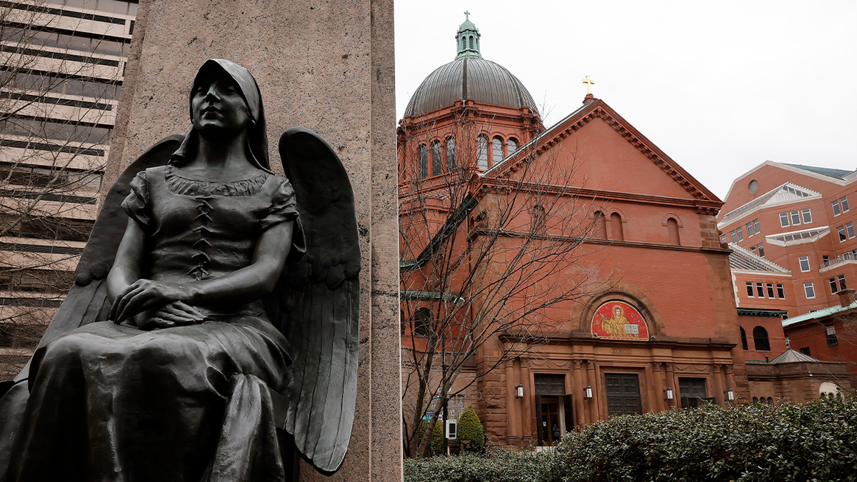 Une statue religieuse au premier plan devant les murs de briques rouges de la cathédrale catholique romaine de Saint Matthieu l'Apôtre