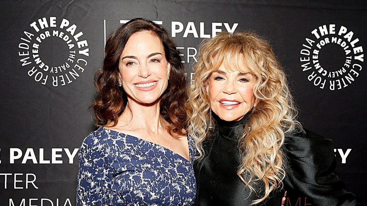 Jennifer Grant en robe bleue et blanche souriante à côté de sa mère Dyan Cannon en costume noir