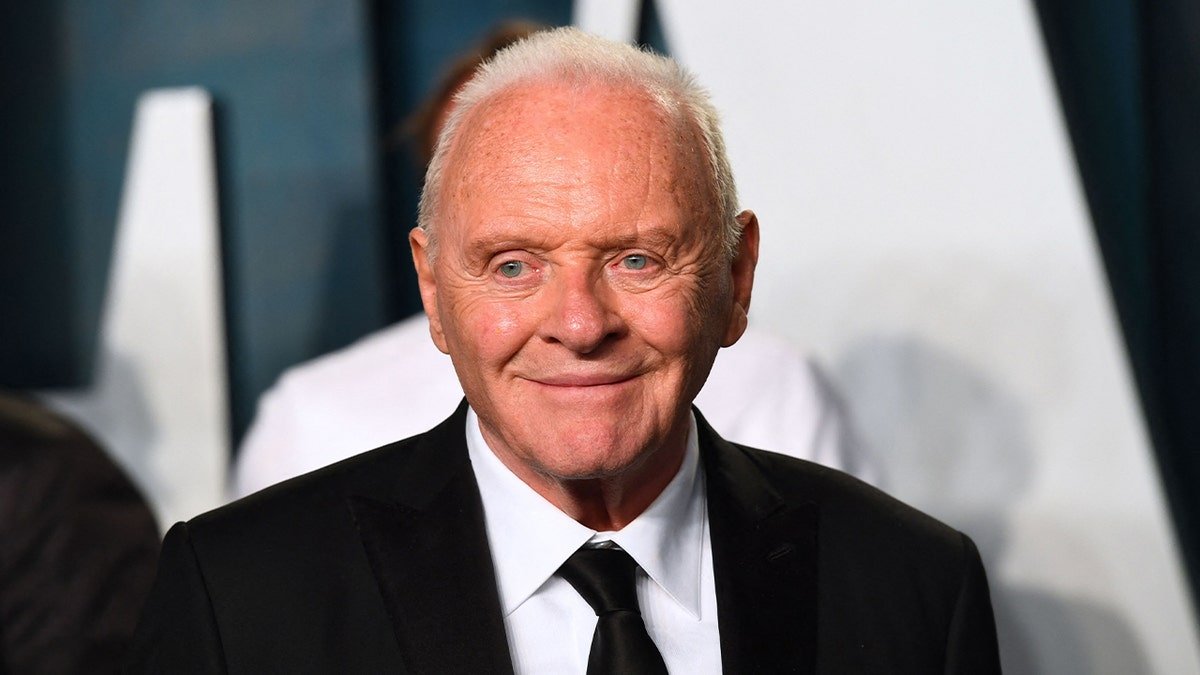 Anthony Hopkins porte un costume noir.