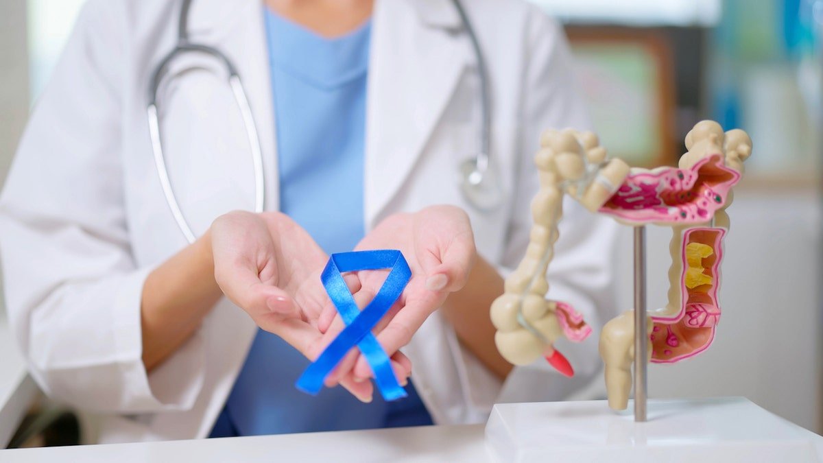 Un médecin avec un ruban bleu à côté d'un modèle de cancer du côlon