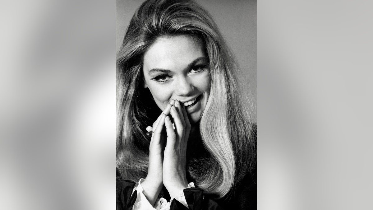 Dyan Cannon souriant dans une pose de prière.