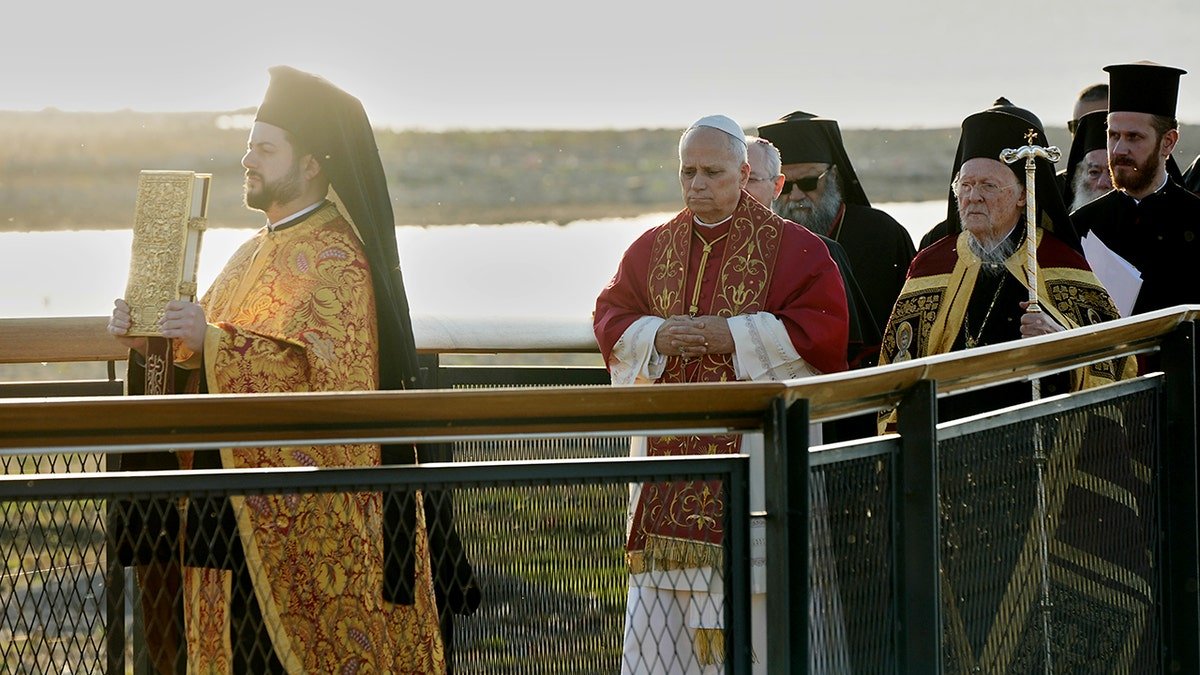 Des religieux vêtus de vêtements ornés marchent dans une procession religieuse le long d'une plate-forme au bord de l'eau.