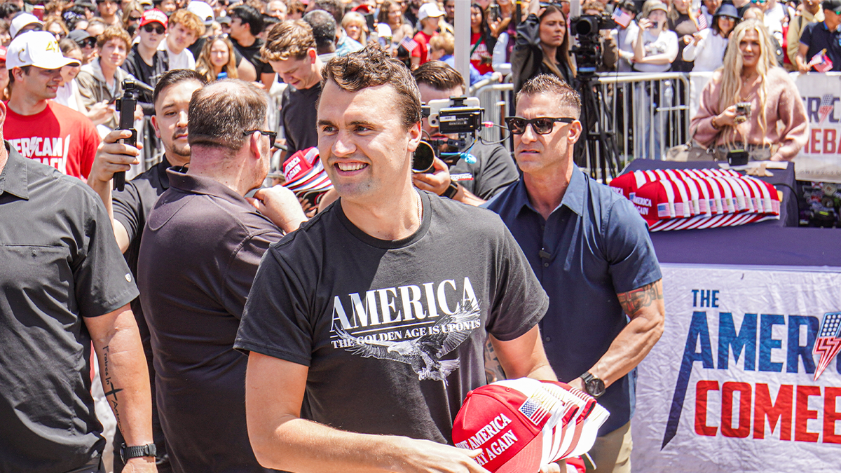 Charlie Kirk souriant en lançant des chapeaux MAGA